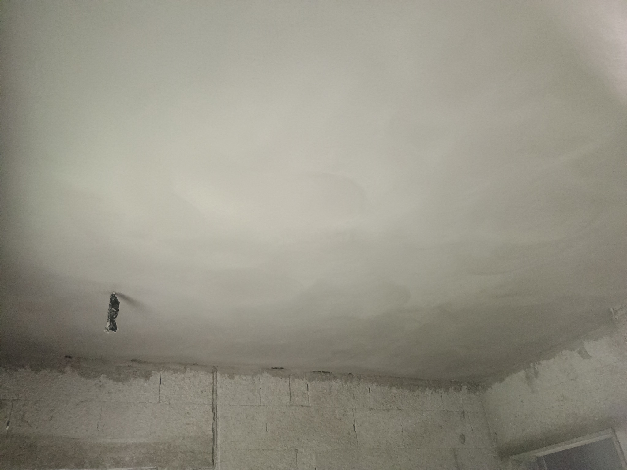 Świeżo położony tynk na suficie i górnej części ściany z widoczną puszką elektryczną w Blanka. Tynk jeszcze mokry, widoczne ślady po szpachli.