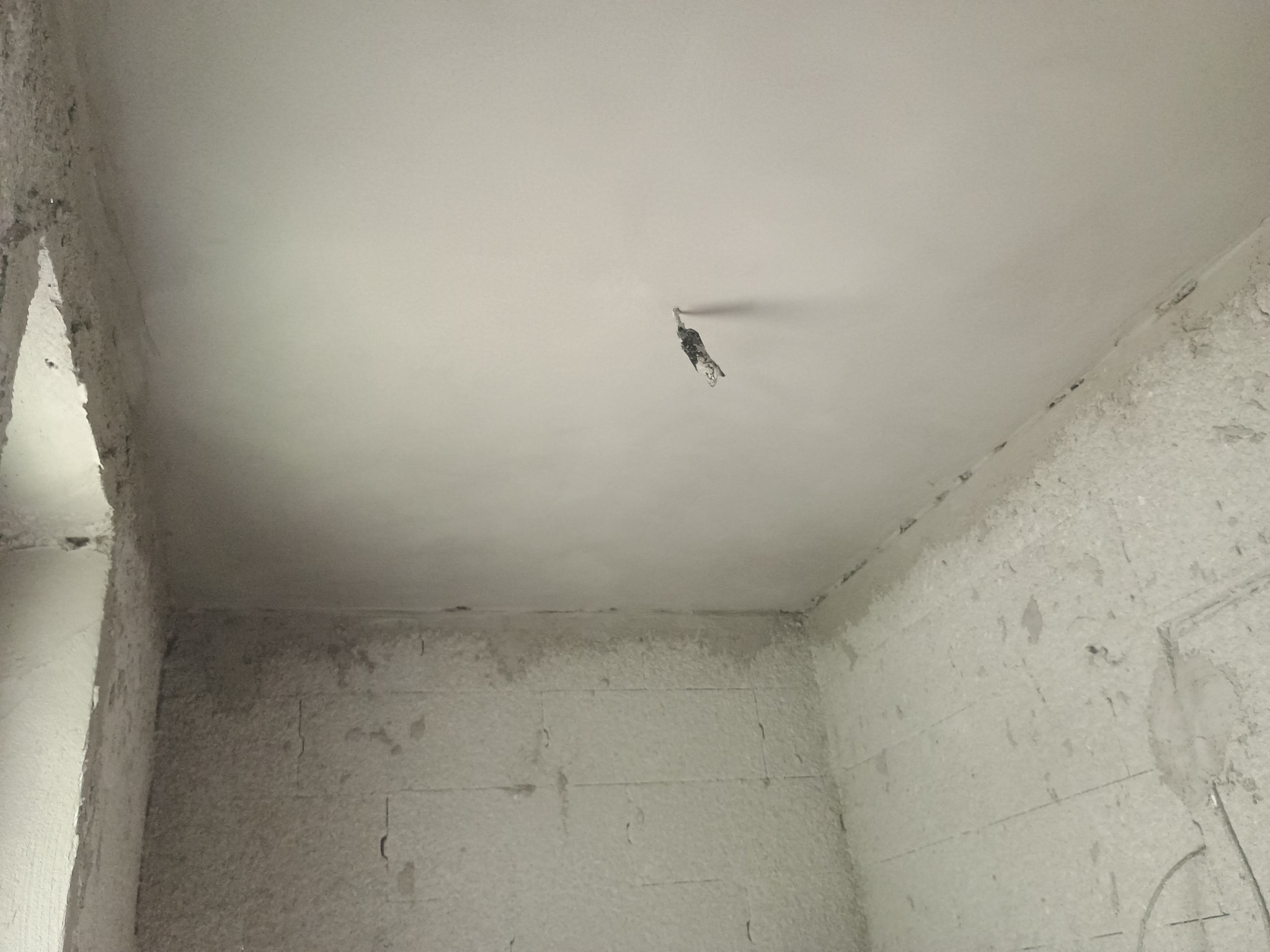 Gładka, świeżo położona jasna warstwa na suficie w surowym wnętrzu, widoczne kable elektryczne wystające z sufitu, ściany z widoczną fakturą bloczków.