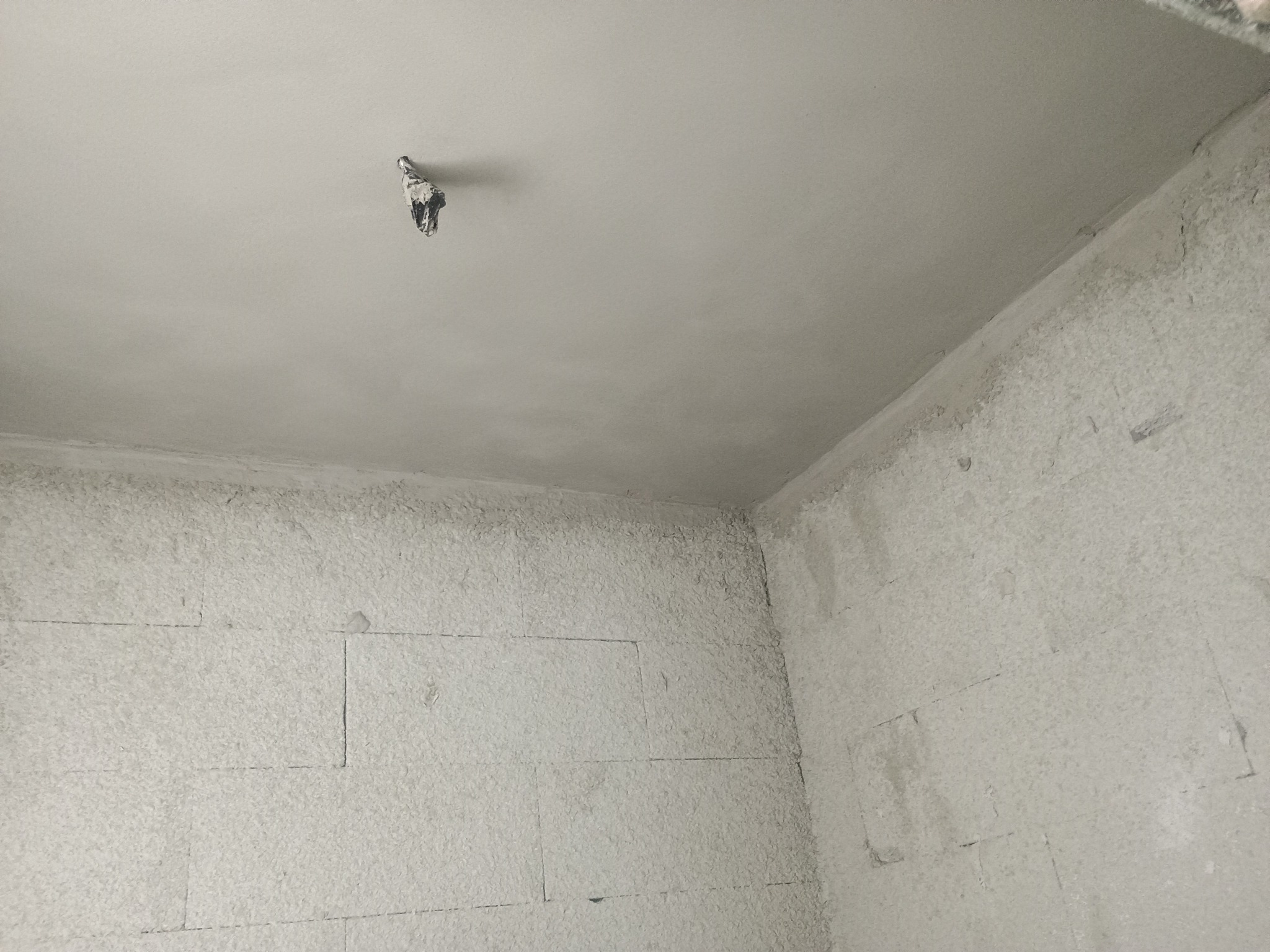 Wnętrze pomieszczenia po nałożeniu świeżego, jasnoszarego tynku, widoczne zabezpieczenie instalacji elektrycznej na suficie.