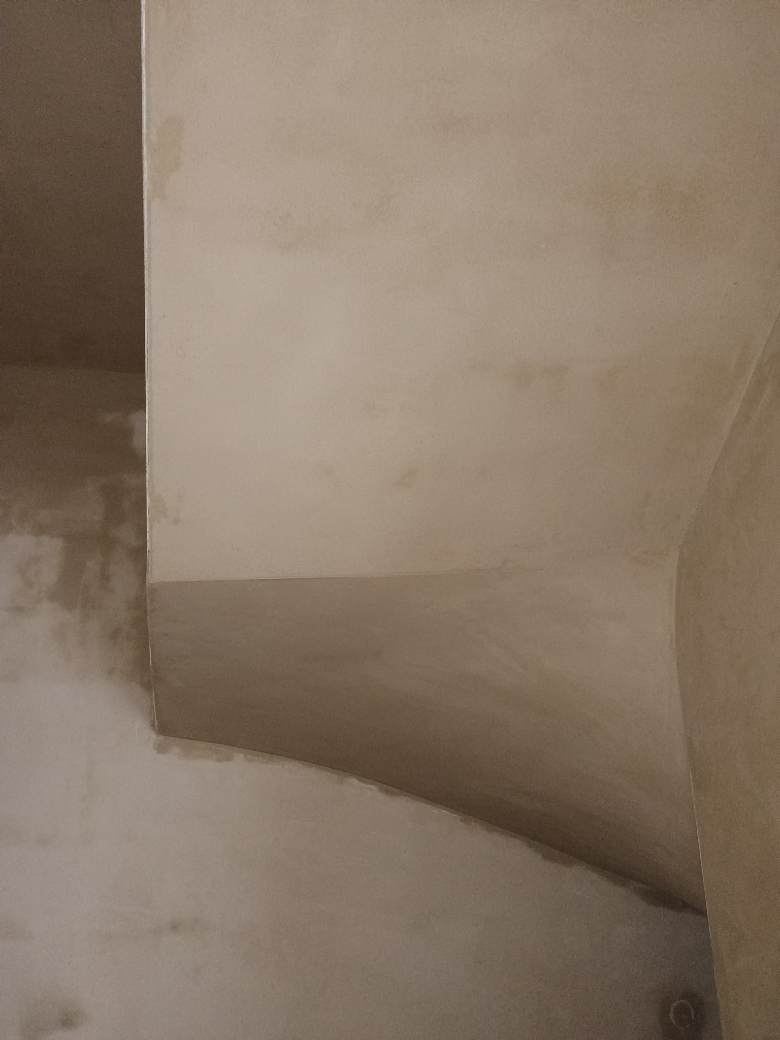 Narożnik wewnętrzny pomieszczenia po nałożeniu jasnej, gładkiej warstwy tynku. Widoczne niedociągnięcia w postaci plam i nierówności na powierzchni. Zauważalny łuk na łączeniu ścian.