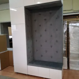 Biała szafa z wnęką wyściełaną szarym materiałem z guzikami, połączona z siedziskiem i szafkami dolnymi.