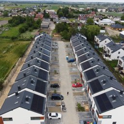 KENPOL Holding Łódź - Widok z lotu ptaka na szereg domów jednorodzinnych z panelami słonecznymi na dachach; w tle zabudowa wiejska i odległe miasto.