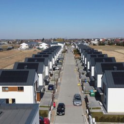 KENPOL Holding Łódź - Widok z lotu ptaka na szereg identycznych, nowoczesnych domów z panelami fotowoltaicznymi na dachach, ustawionych wzdłuż ulicy osiedlowej w słoneczny dzień.