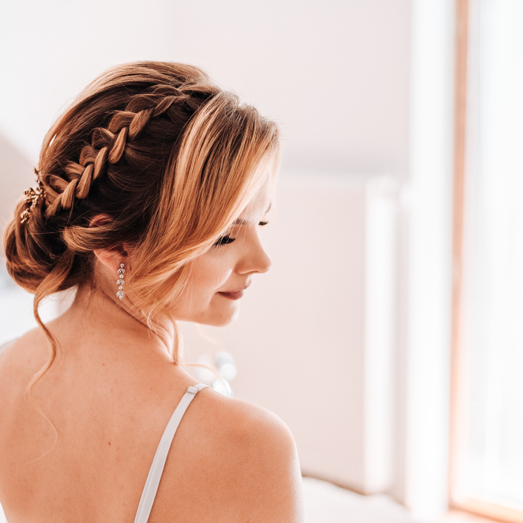 Profil kobiety z upiętymi włosami w warkocz, ozdobionymi złotymi spinkami i długimi, wiszącymi kolczykami.