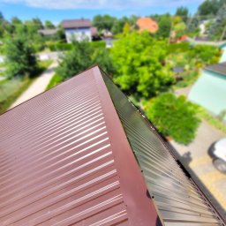 Firma Dekarska - Nowe, brązowe pokrycie dachowe z blachy trapezowej widziane z góry, z widokiem na okoliczne domy i zieleń w tle.