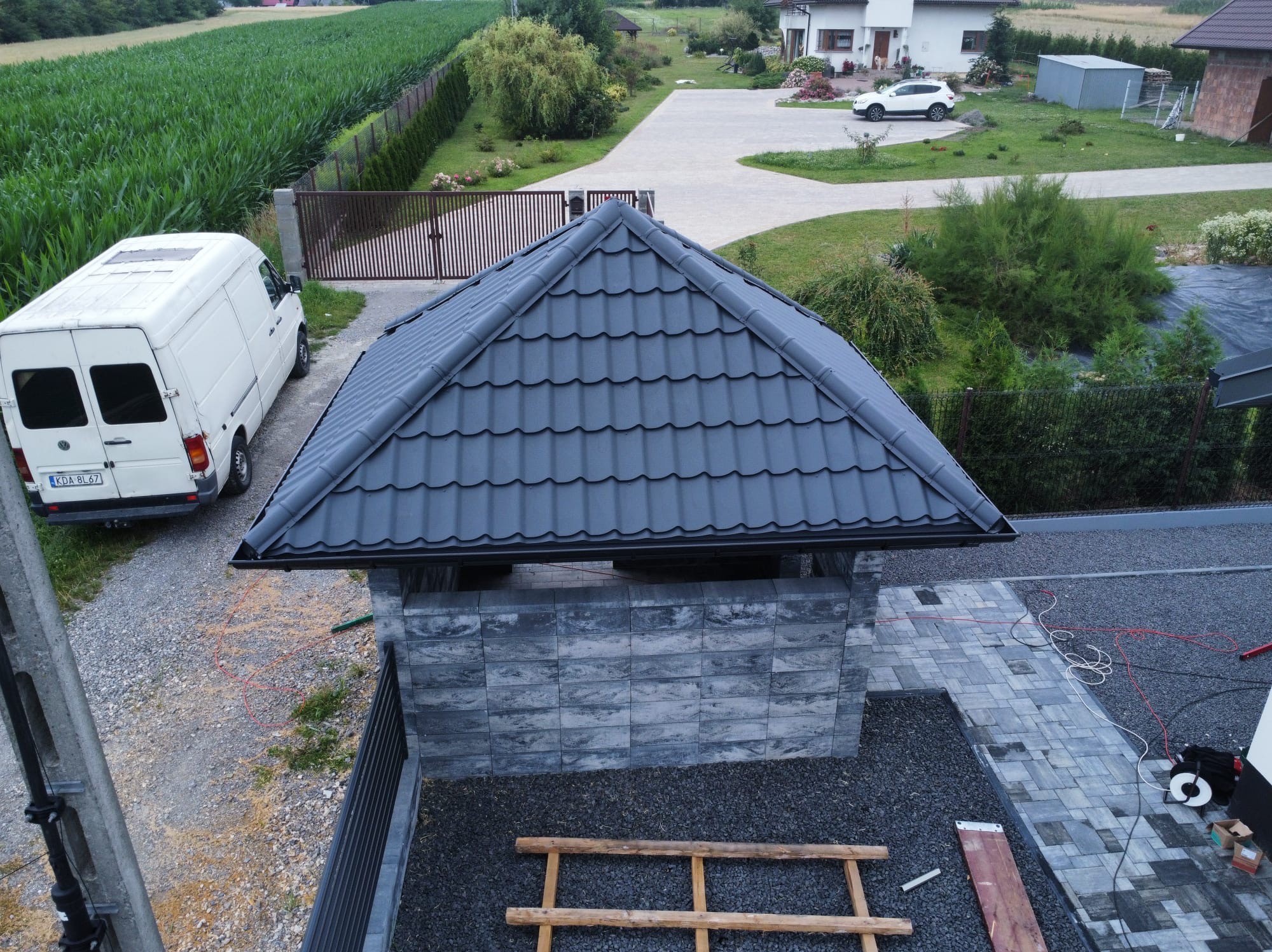 Nowoczesna, grafitowa konstrukcja z dachówką ceramiczną w ogrodzie, widok z góry, z bliska widoczny fragment dachu, w tle zabudowania mieszkalne i zaparkowany biały bus