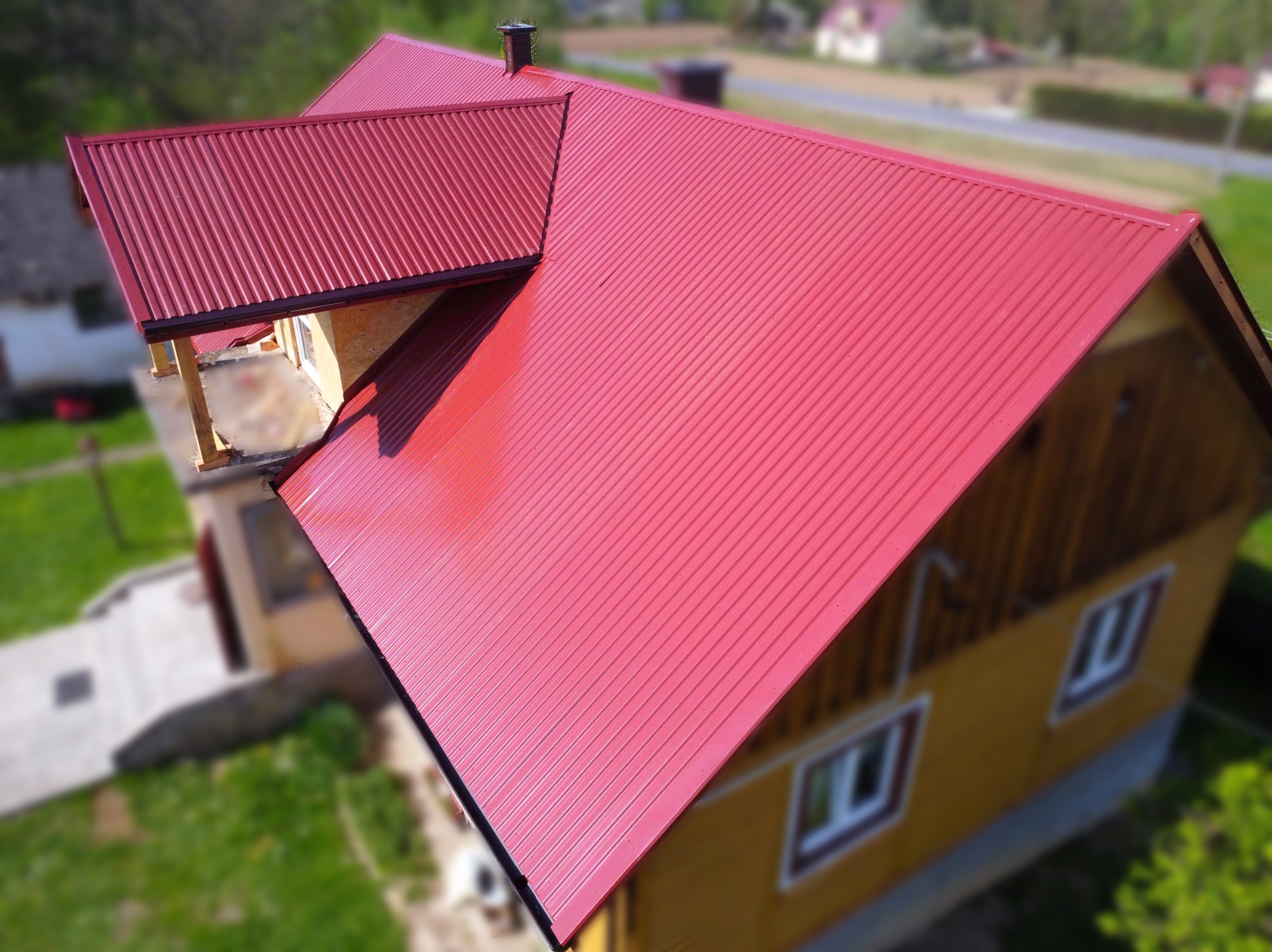 Czerwony, blaszany dach z widocznymi liniami łączeń, świeżo położony na drewnianym domu z widokiem z góry.