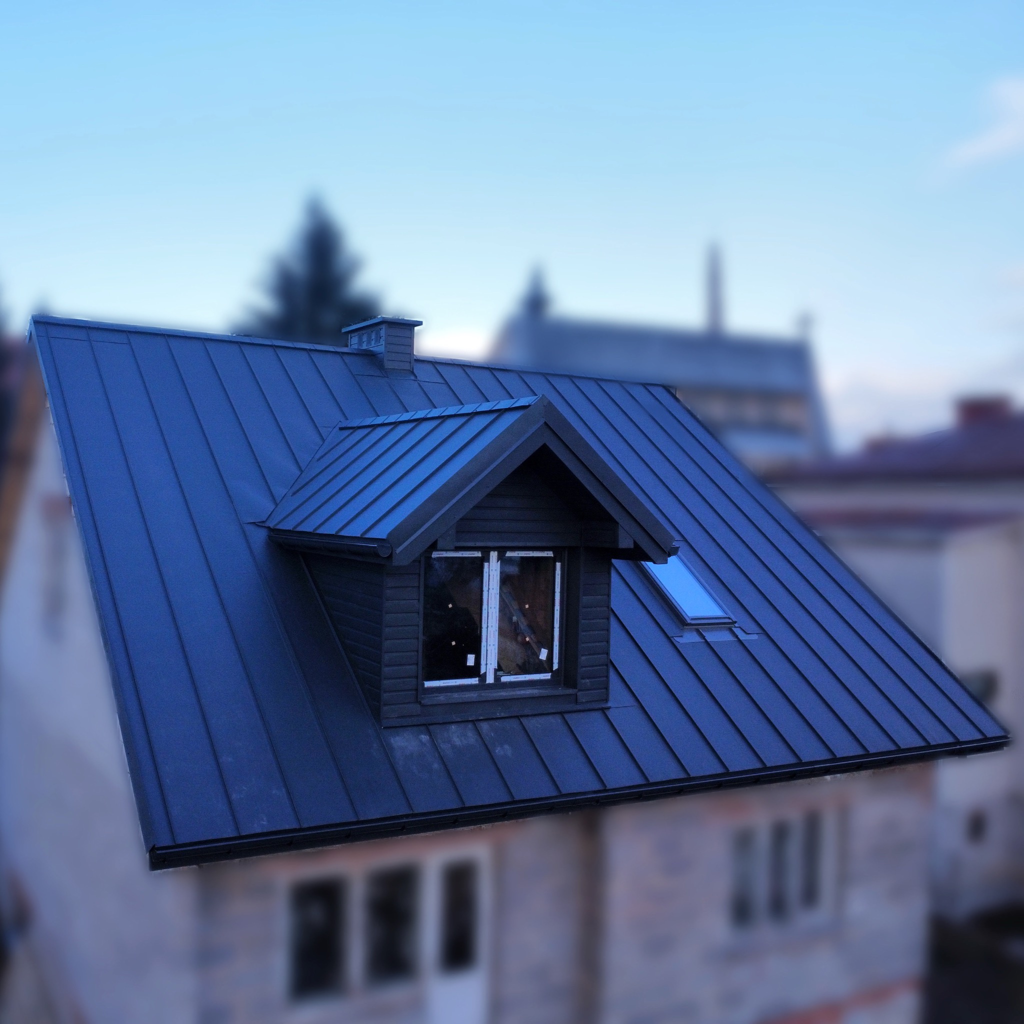 Nowoczesny dach z blachy na domu jednorodzinnym z lukarną i oknem dachowym, widoczne detale orynnowania i komin