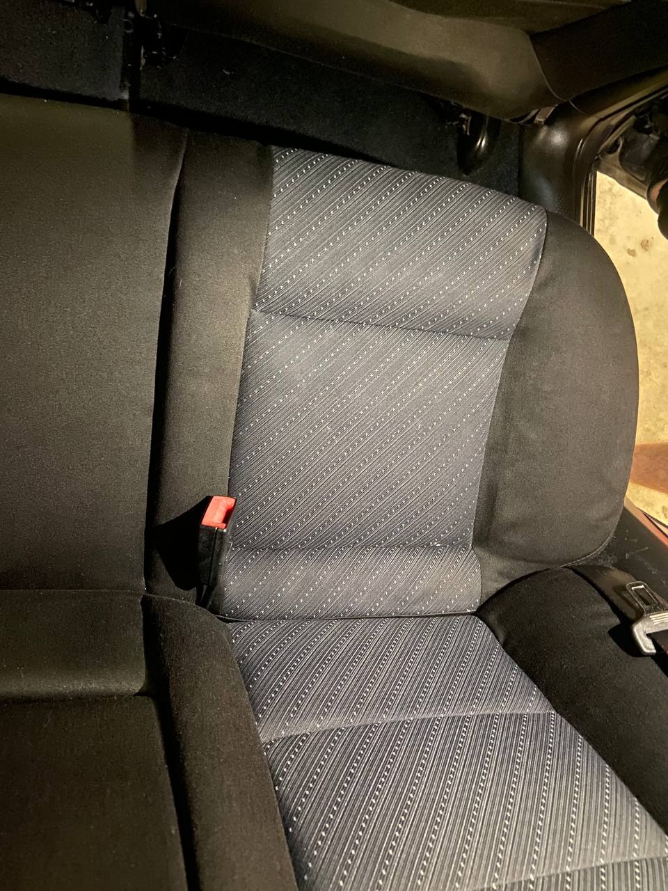 Szare, wzorzyste obicie fotela samochodowego z widocznym czerwonym elementem pasa bezpieczeństwa.