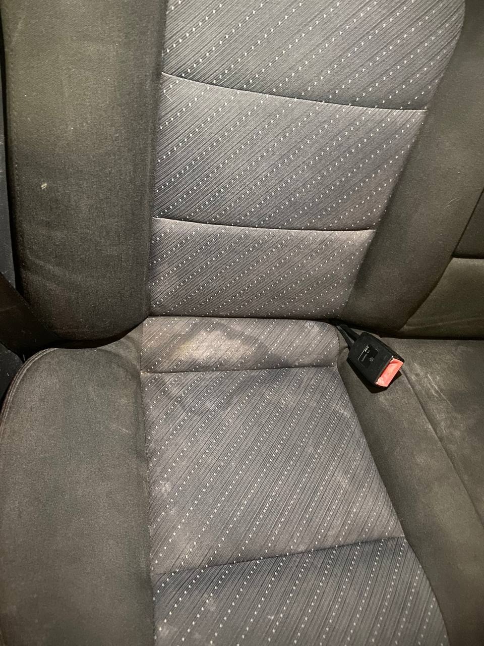 Zabrudzone siedzisko fotela samochodowego z pasami bezpieczeństwa, wymagające czyszczenia, widoczne plamy na tapicerce w Warszawie.