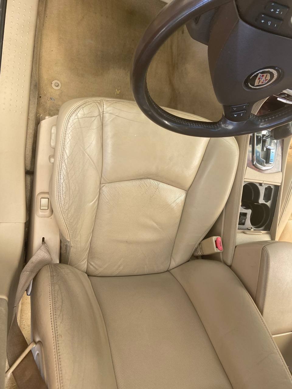 Beżowe skórzane siedzenie samochodowe z widocznymi śladami użytkowania i pęknięciami, uchwycone z góry, z fragmentem kierownicy i konsoli środkowej w tle.