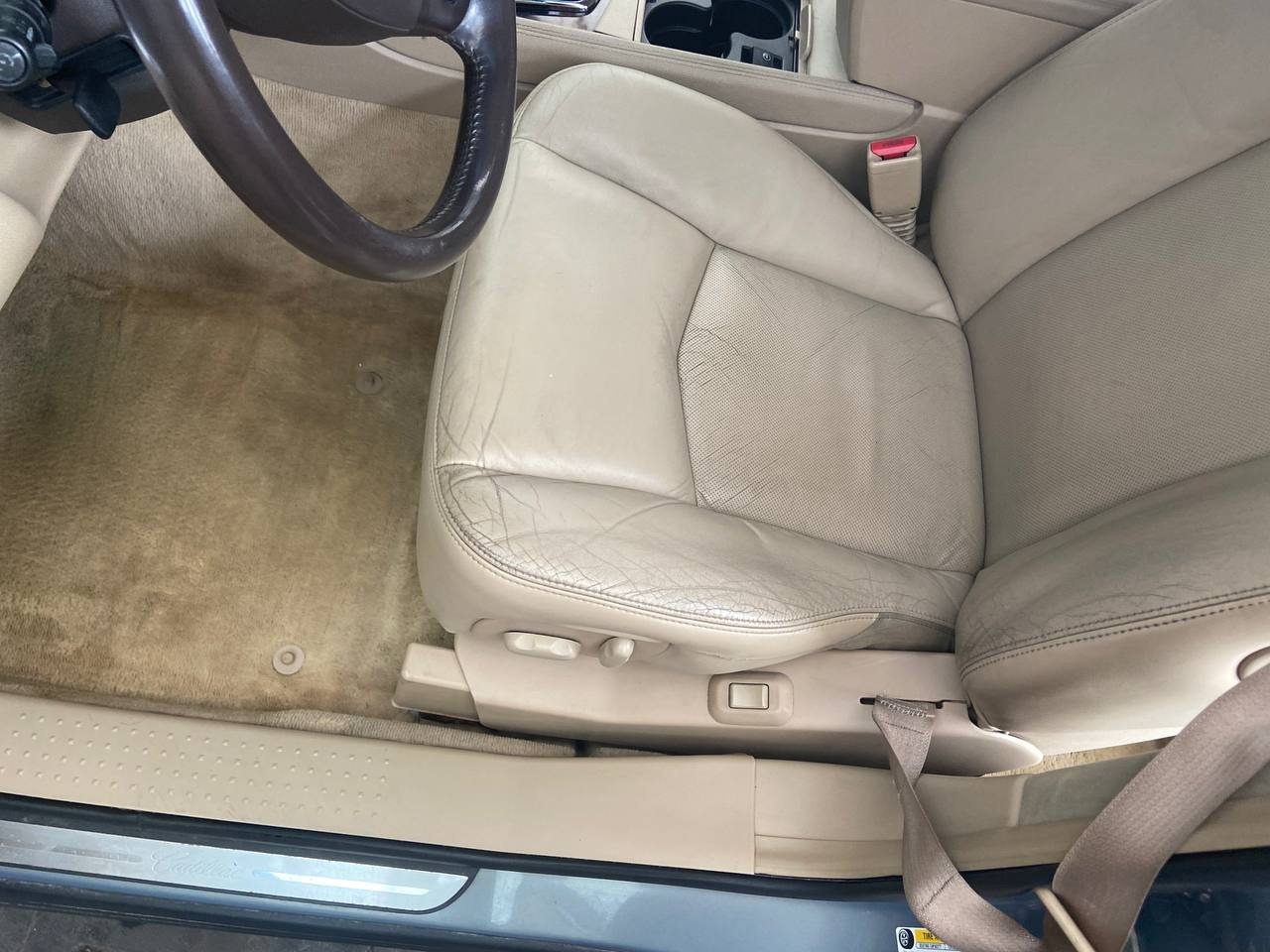 Beżowa skórzana tapicerka fotela samochodowego z widocznymi śladami użytkowania i zabrudzeniami na siedzisku oraz dywaniku podłogowym.