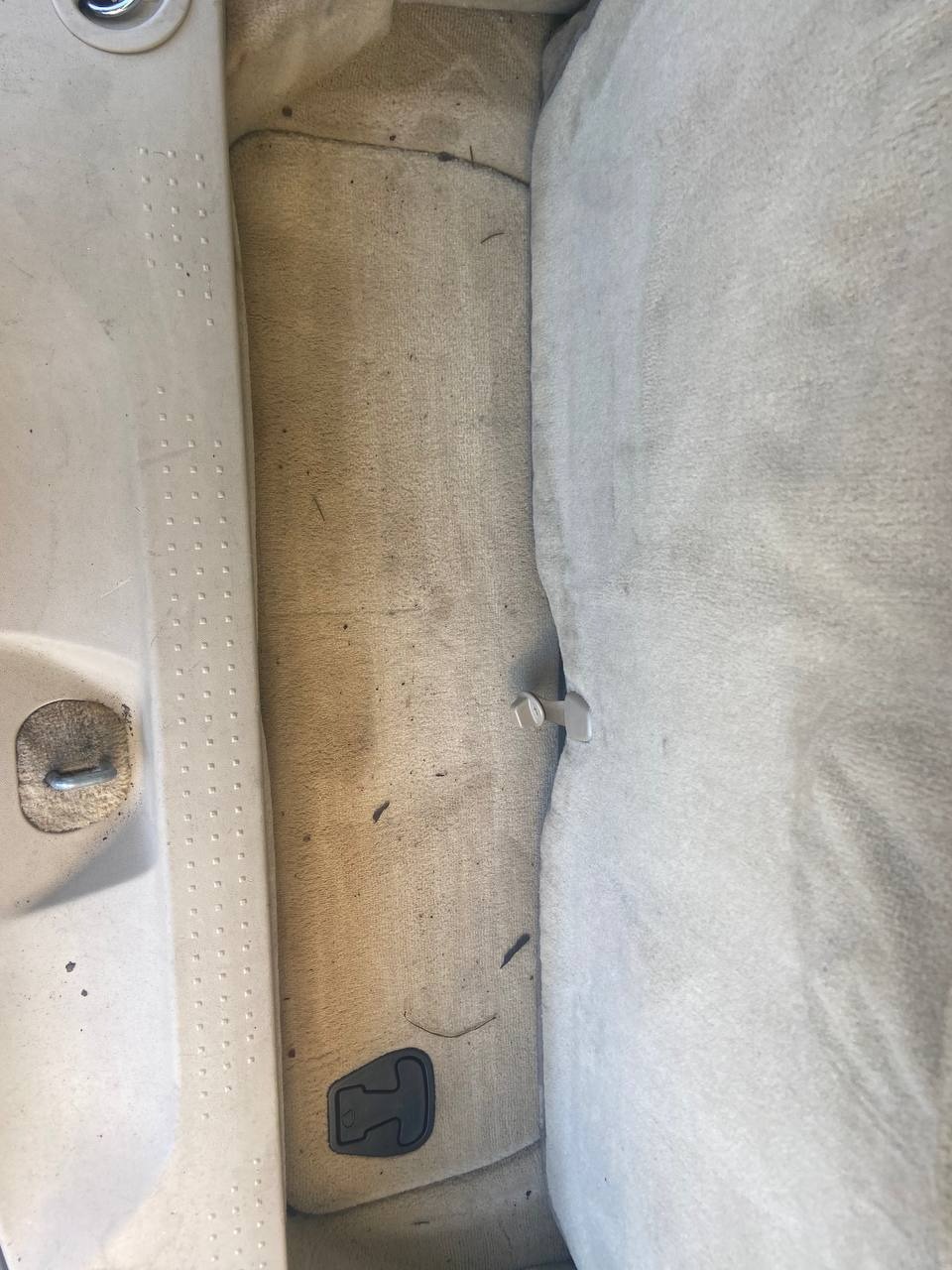 Brudna, beżowa tapicerka samochodowa z widocznymi plamami i zanieczyszczeniami, fragment siedzenia i podłogi pojazdu przed czyszczeniem.