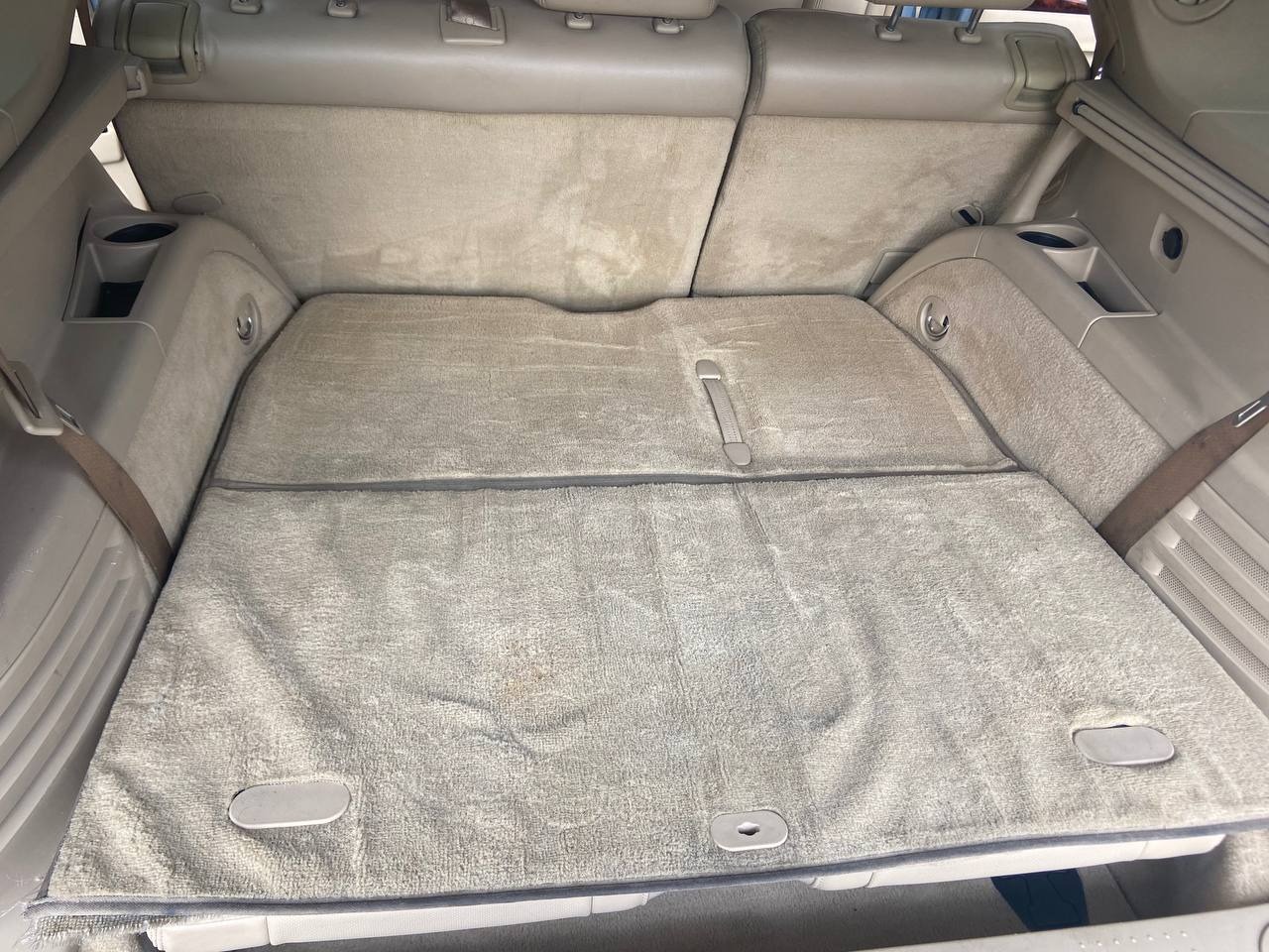 Widok bagażnika samochodu SUV z beżową tapicerką, dywanikiem i widocznymi plamami.
