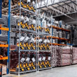 Magazyn pełen nowych, żółto-czarnych wózków paletowych elektrycznych na metalowych regałach, widok z perspektywy podłogi, oświetlenie magazynowe.