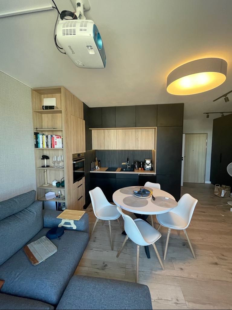 Nowoczesne wnętrze z aneksem kuchennym, okrągłym stołem i projektorem zamontowanym na suficie, oświetlenie punktowe.