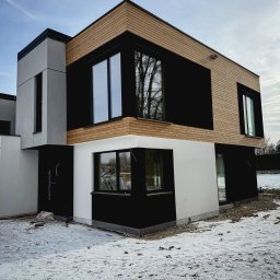 Karsbud - Nowoczesny dom z elewacją w kolorach bieli, czerni i drewna. Widoczne okna i fragment ogrodu pokrytego śniegiem. Minimalistyczny design i geometryczne kształty.