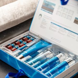 BRUNON FIDRYCH - Zestaw kosmetyków Intraceuticals w otwartym, błękitnym pudełku, prezentujący ampułki, tubkę i buteleczki z srebrnymi aplikatorami, z widoczną ulotką informacyjną w tle.