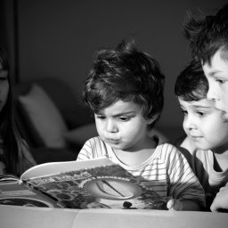 BRUNON FIDRYCH - Czarno-białe zdjęcie czwórki dzieci skupionych na czytaniu książki z magnetyczną zabawką, dziewczynka z długimi włosami po lewej, chłopiec w paski na środku, dwaj chłopcy w koszulach po prawej.