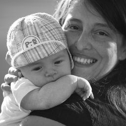 BRUNON FIDRYCH - Czarno-białe zdjęcie uśmiechniętej kobiety trzymającej na rękach niemowlę w czapce w kratę w Warszawie.