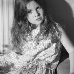 BRUNON FIDRYCH - Portret czarno-biały dziewczynki w kwiecistej sukience, oparta o betonową ścianę, oświetlona bocznym światłem.