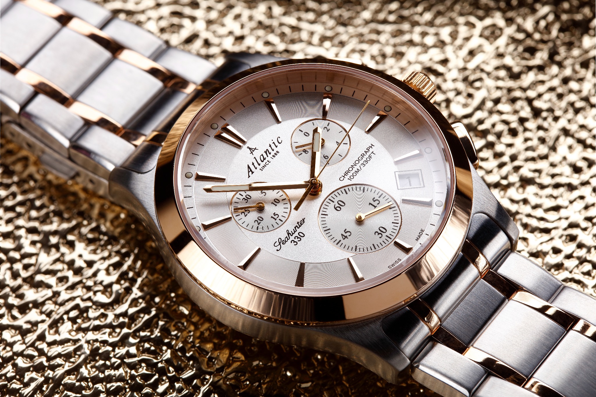 Zegarek Atlantic Seahunter 330 z metalową bransoletą w kolorze srebrno-złotym na teksturowanym złotym tle.