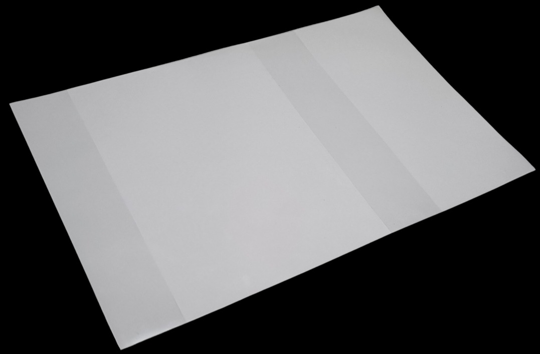 Rozłożony, biały karton z trzema panelami, z widocznymi liniami zagięć, na czarnym tle.