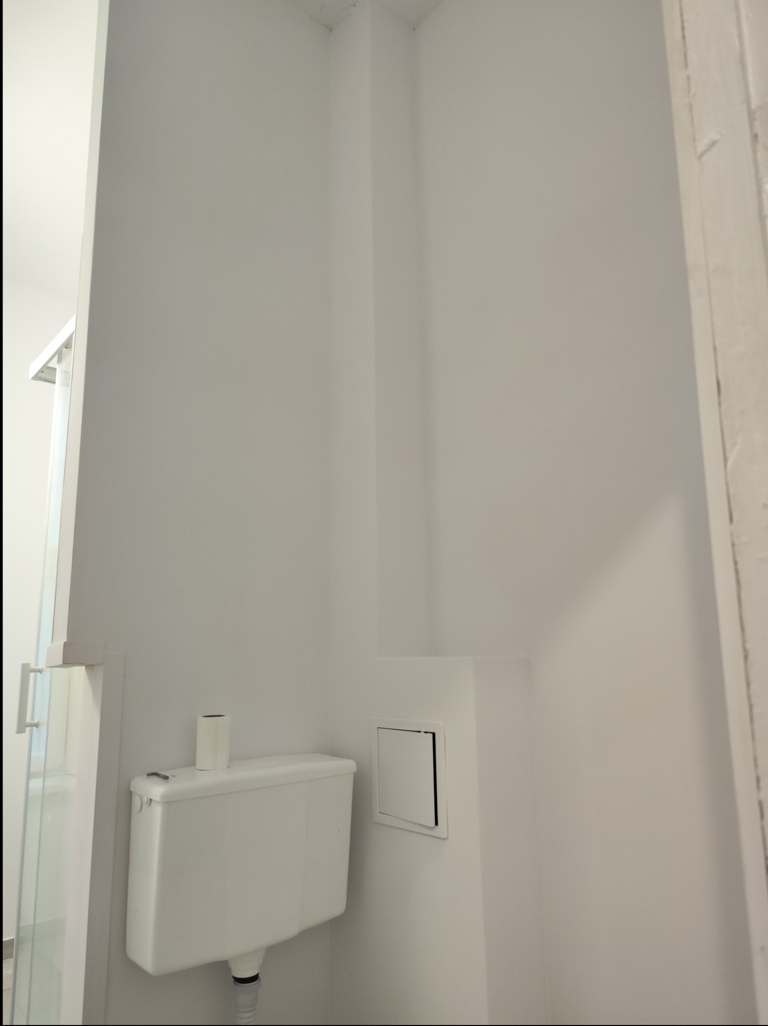 Biała, świeżo pomalowana ściana w łazience z zamontowaną toaletą i widoczną kabiną prysznicową w tle.