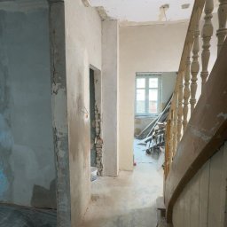 USŁUGI BUDOWLANE- OSKAR DULĘBA - Wnętrze w trakcie remontu: przygotowane ściany do malowania, widoczne instalacje, podłoga zabezpieczona folią, schody z drewnianą balustradą. Prace wykończeniowe.