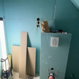 Montaż płyt karton-gips na poddaszu ze skośnym sufitem. Widoczne narzędzia, instalacja elektryczna i sanitarna. Oświetlenie halogenowe.