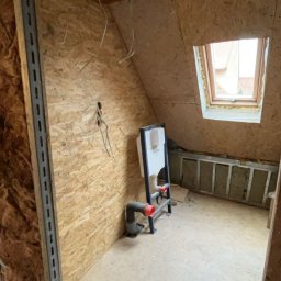 USŁUGI BUDOWLANE- OSKAR DULĘBA - Adaptacja poddasza: montaż stelaża WC na tle ścian z płyty OSB, widoczne przewody instalacyjne i okno dachowe. Prace wykończeniowe w trakcie.