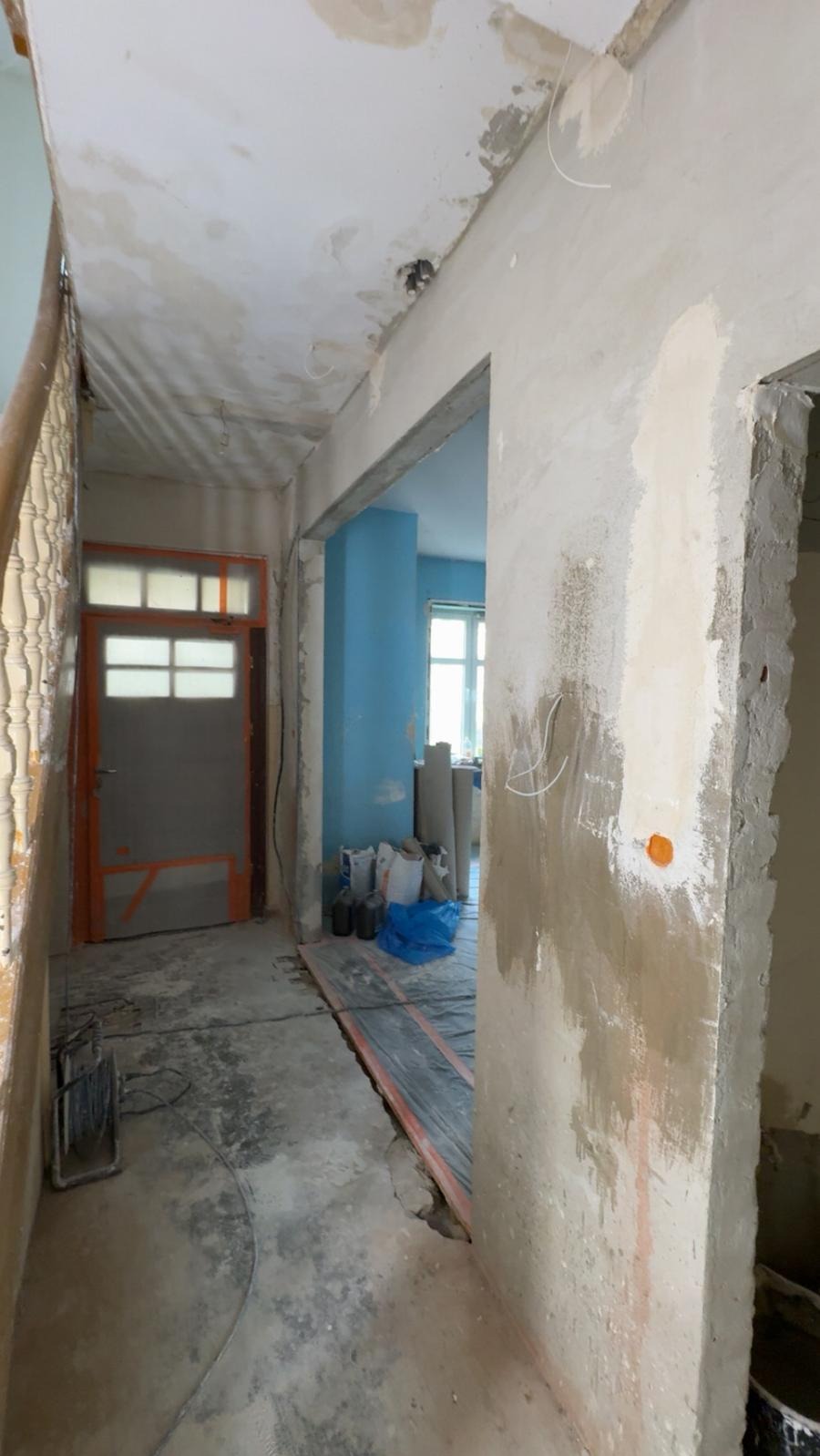 Wnętrze w trakcie remontu: surowe ściany z widocznymi śladami szpachlowania, odkryta instalacja podłogowa, materiały budowlane w tle, przygotowanie do dalszych prac wykończeniowych.