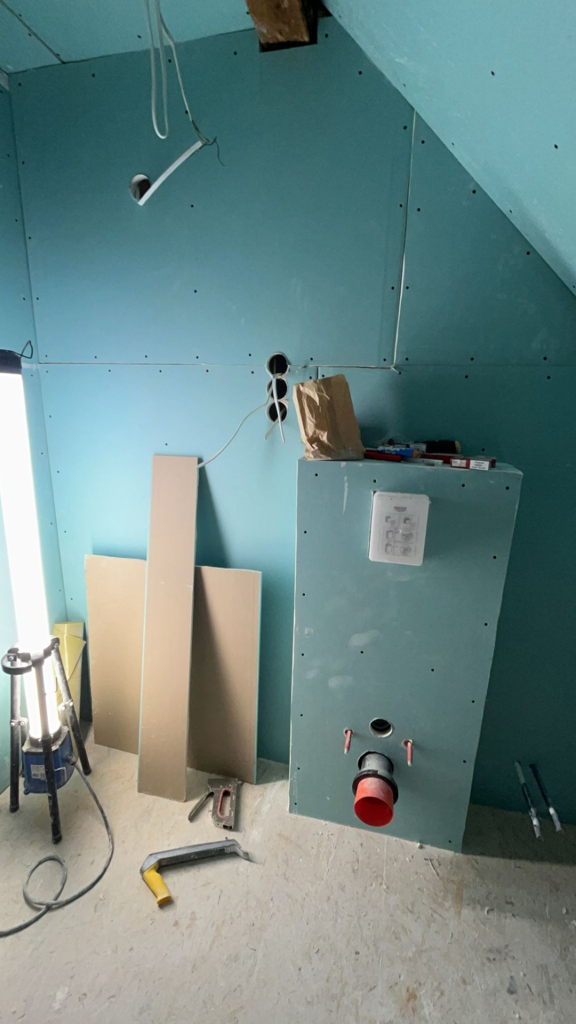 Montaż płyt karton-gips na poddaszu ze skośnym sufitem. Widoczne narzędzia, instalacja elektryczna i sanitarna. Oświetlenie halogenowe.