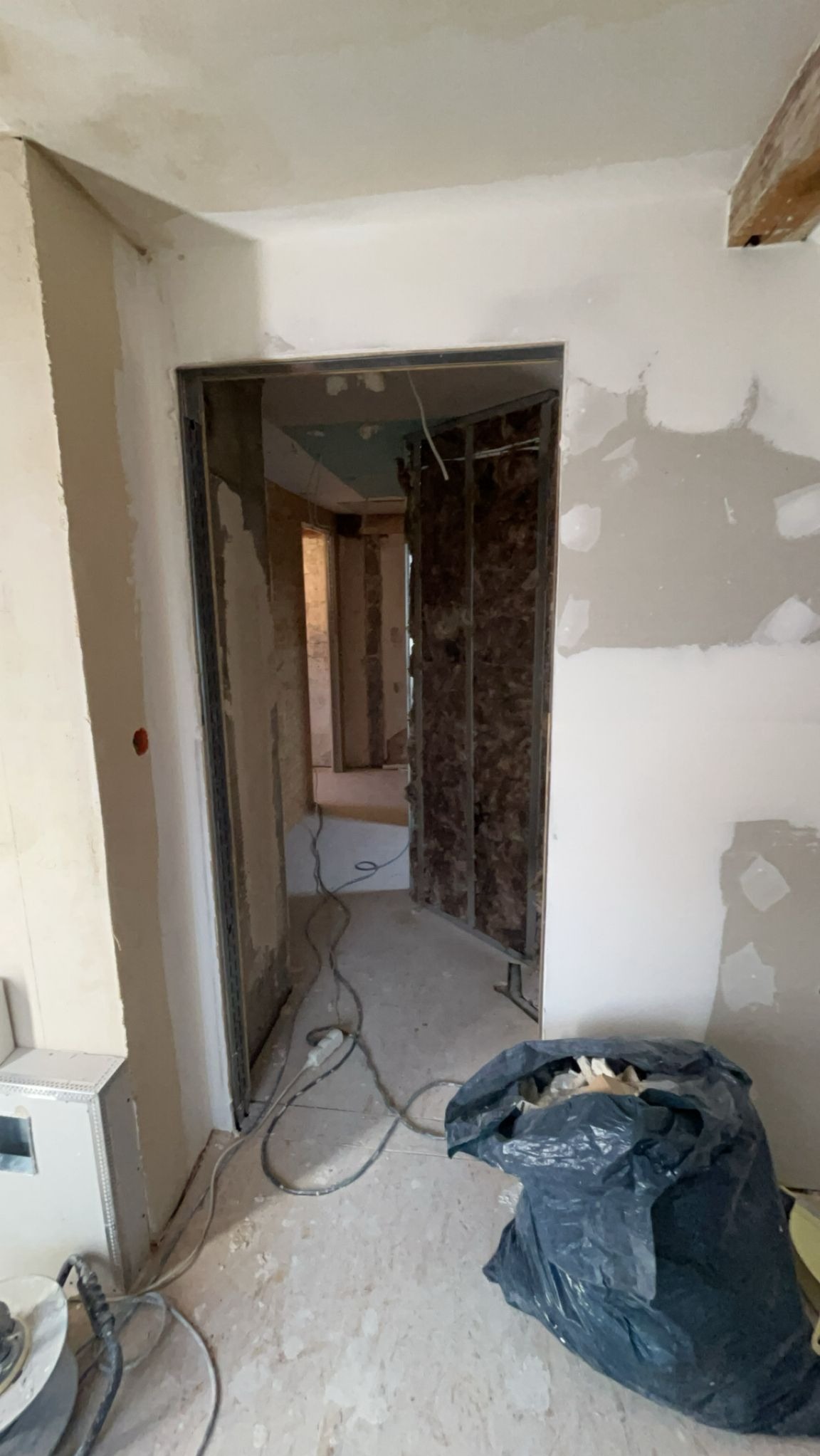 Wnętrze w trakcie prac: ściany przygotowane pod gładzie, widoczne profile i izolacja. Na podłodze kabel i worek z odpadami budowlanymi.