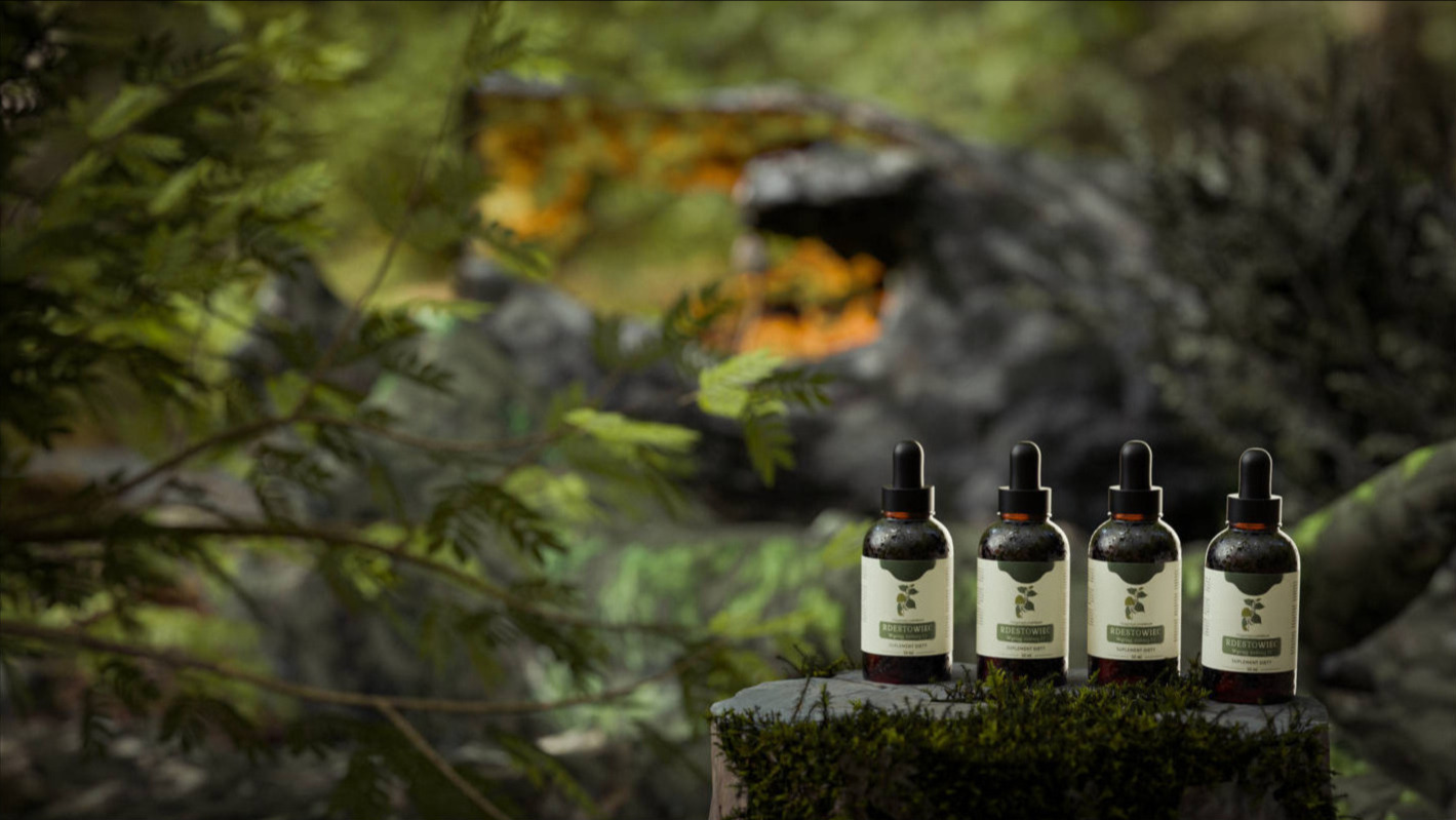 Cztery buteleczki z pipetami, etykietowane z motywem roślinnym, ustawione na mchu na tle leśnym z kamieniami i zielenią.