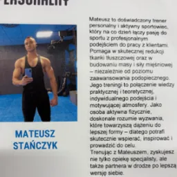 Przystojny trener personalny z Pruszkowa prezentuje sylwetkę na tle siłowni, trzymając telefon. Widoczny napis 'Trener Personalny' i logo 'Zdrofit'.