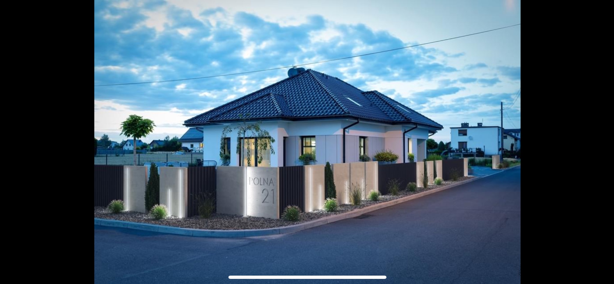 Nowoczesny dom jednorodzinny z podświetlonym ogrodzeniem z elementami betonowymi i metalowymi, ozdobiony niskimi krzewami i małymi drzewkami, widoczny z ulicy o zmierzchu.