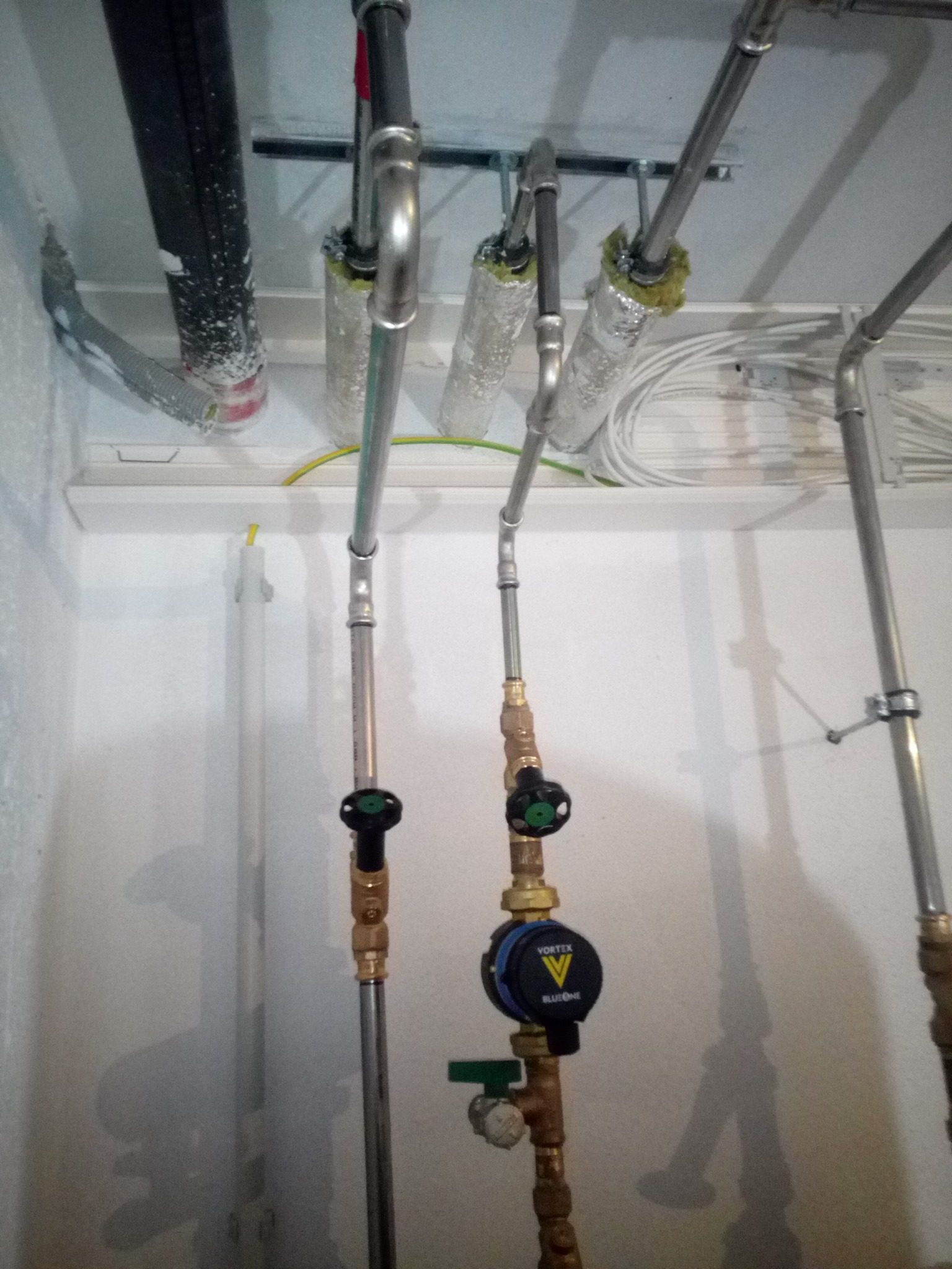 Instalacja hydrauliczna z rur miedzianych i zaworów Vortex BlueOne, widoczne izolowane rury pod stropem, przewody elektryczne i elementy mocujące.
