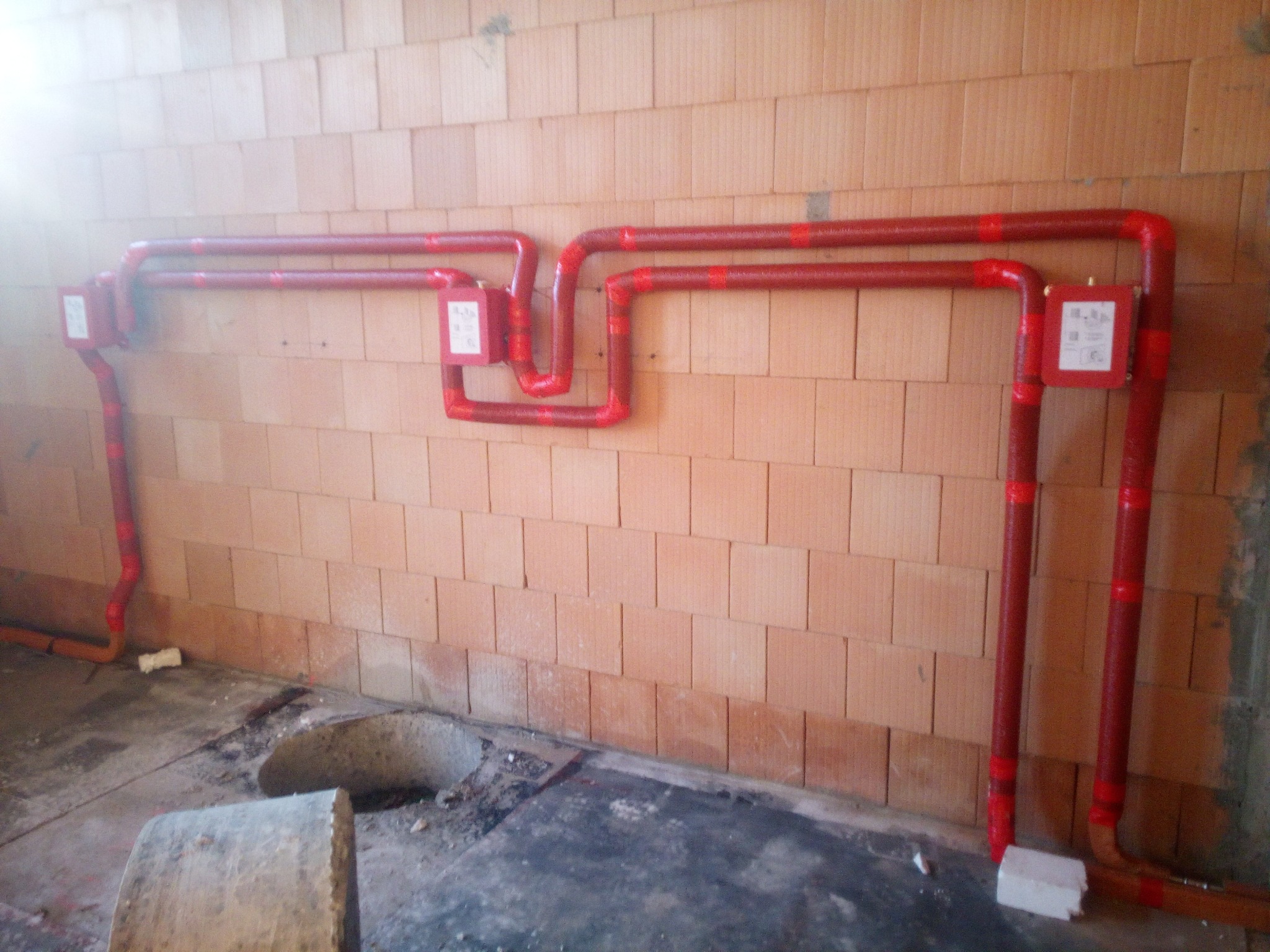 Czerwone rury instalacji grzewczej, zabezpieczone taśmą, zamontowane na ścianie z cegieł dziurawki w surowym stanie.
