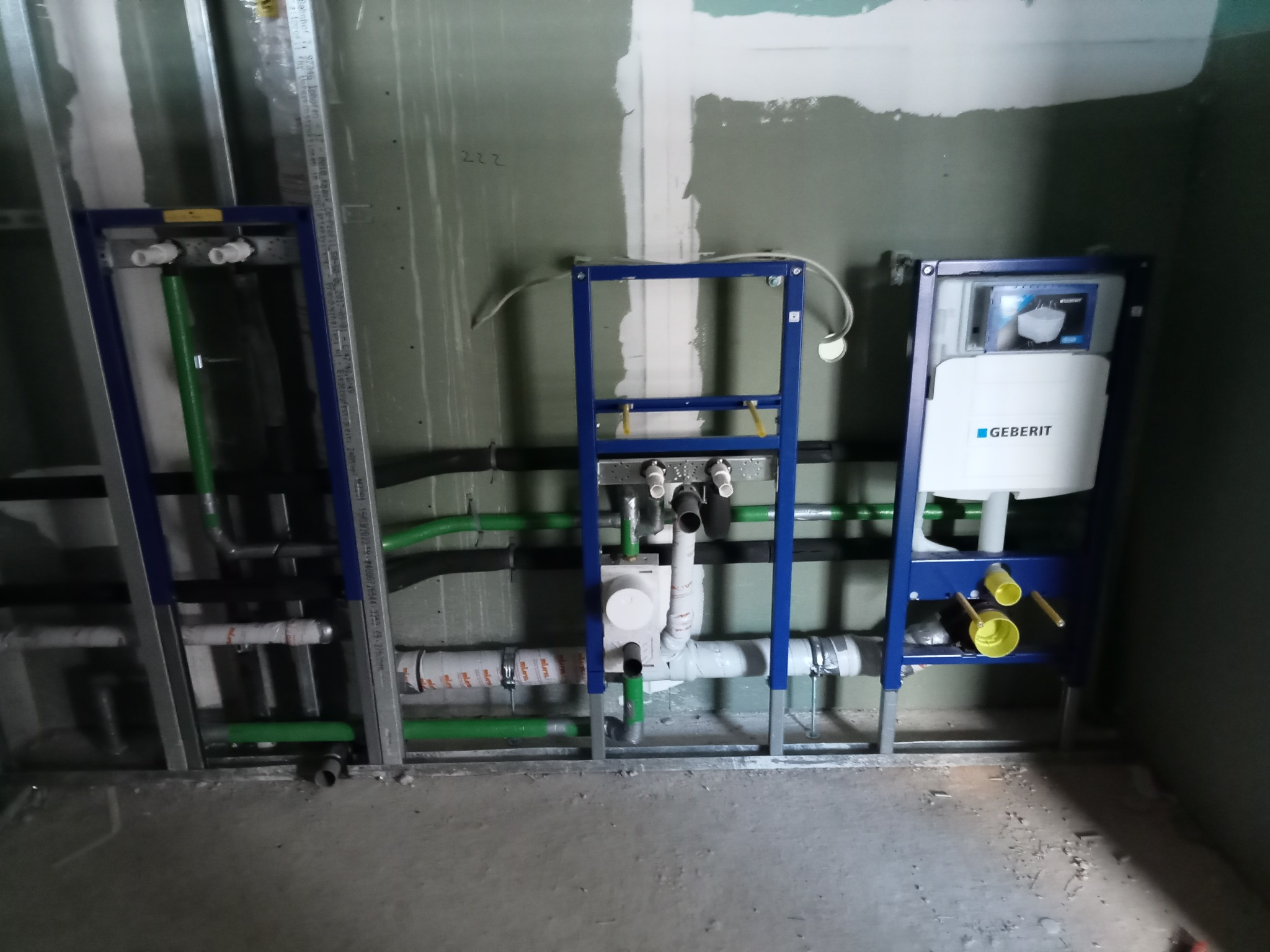 Stelaż podtynkowy Geberit zamontowany na ścianie z widocznymi rurami instalacji wodnej i kanalizacyjnej w trakcie montażu, na surowej ścianie z widocznymi śladami gipsu.