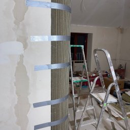 Katarzyna Trofiniak - Przygotowanie do gładzi: kolumna z siatką mocowaną taśmą, drabiny w tle. Prace wykończeniowe w mieszkaniu w Warszawie. Nietypowe rozwiązanie.