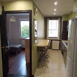 Katarzyna Trofiniak - Wnętrze mieszkania po remoncie: widok z salonu na kuchnię z rozkładanym stołem i krzesłami, ciemna podłoga w salonie kontrastuje z jasną w kuchni.