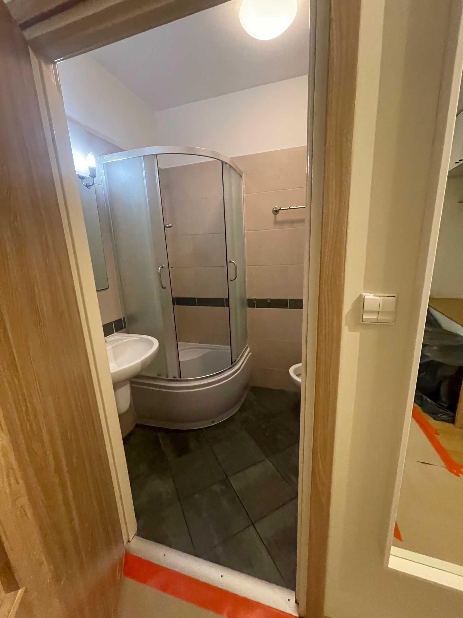 Wykończona łazienka z kabiną prysznicową i umywalką, widok zza futryny drzwi. Ciemna podłoga. Usługi remontowe w Warszawie.