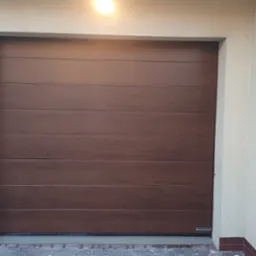 Zamknięta, brązowa, segmentowa brama garażowa z poziomymi panelami, marki Hormann, widoczna od frontu, wnęka wykończona jasnym tynkiem.