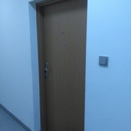 DG SPÓŁKA Z OGRANICZONĄ ODPOWIEDZIALNOŚCIĄ - Brązowe drzwi wejściowe do mieszkania z numerem 97 i panelem domofonu na ścianie.