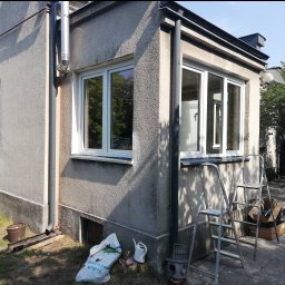 DG SPÓŁKA Z OGRANICZONĄ ODPOWIEDZIALNOŚCIĄ - Narożne ujęcie domu z nowymi białymi oknami, widoczne drabiny i materiały budowlane sugerują trwający montaż.