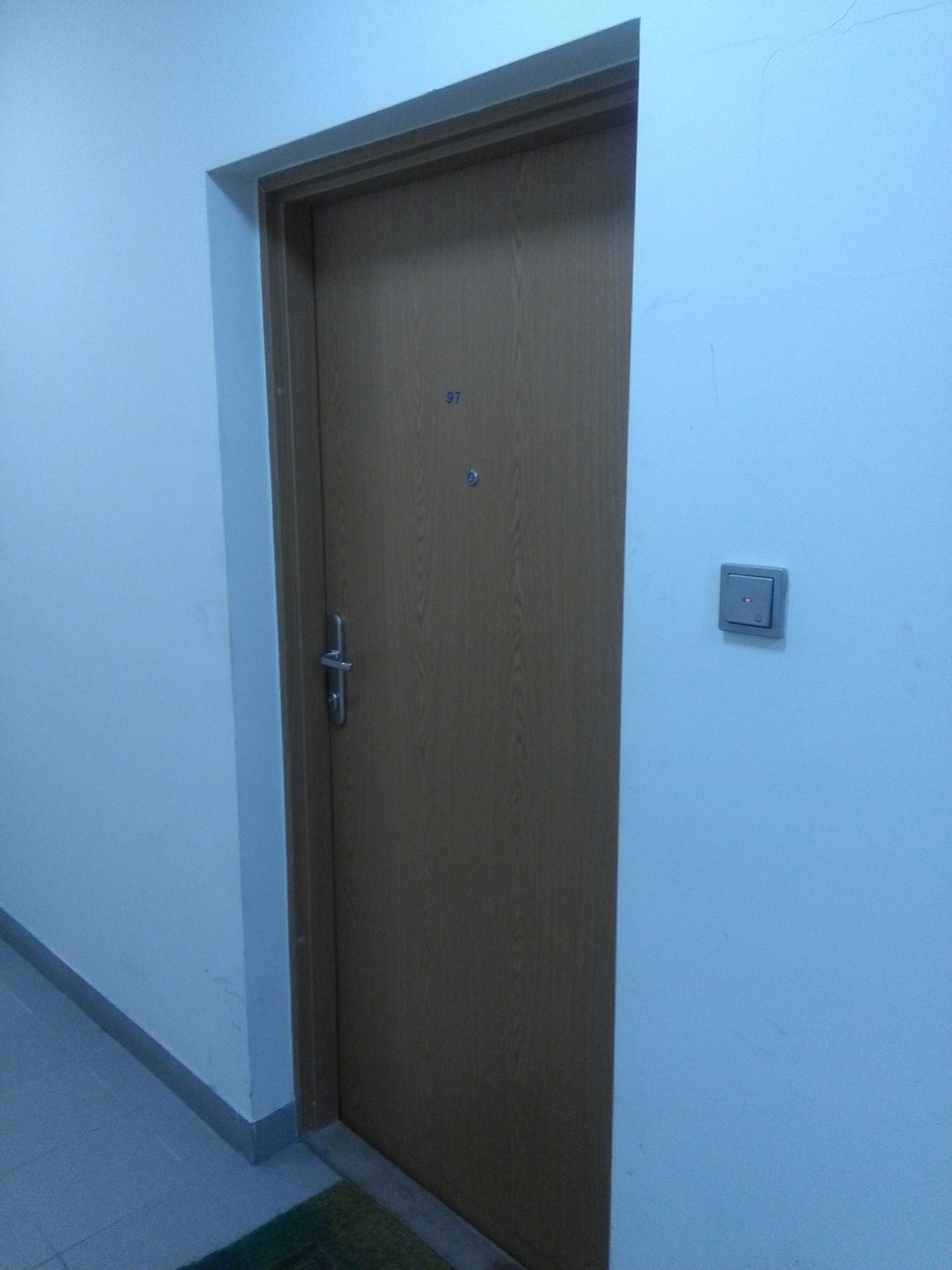 Brązowe drzwi wejściowe do mieszkania z numerem 97 i panelem domofonu na ścianie.
