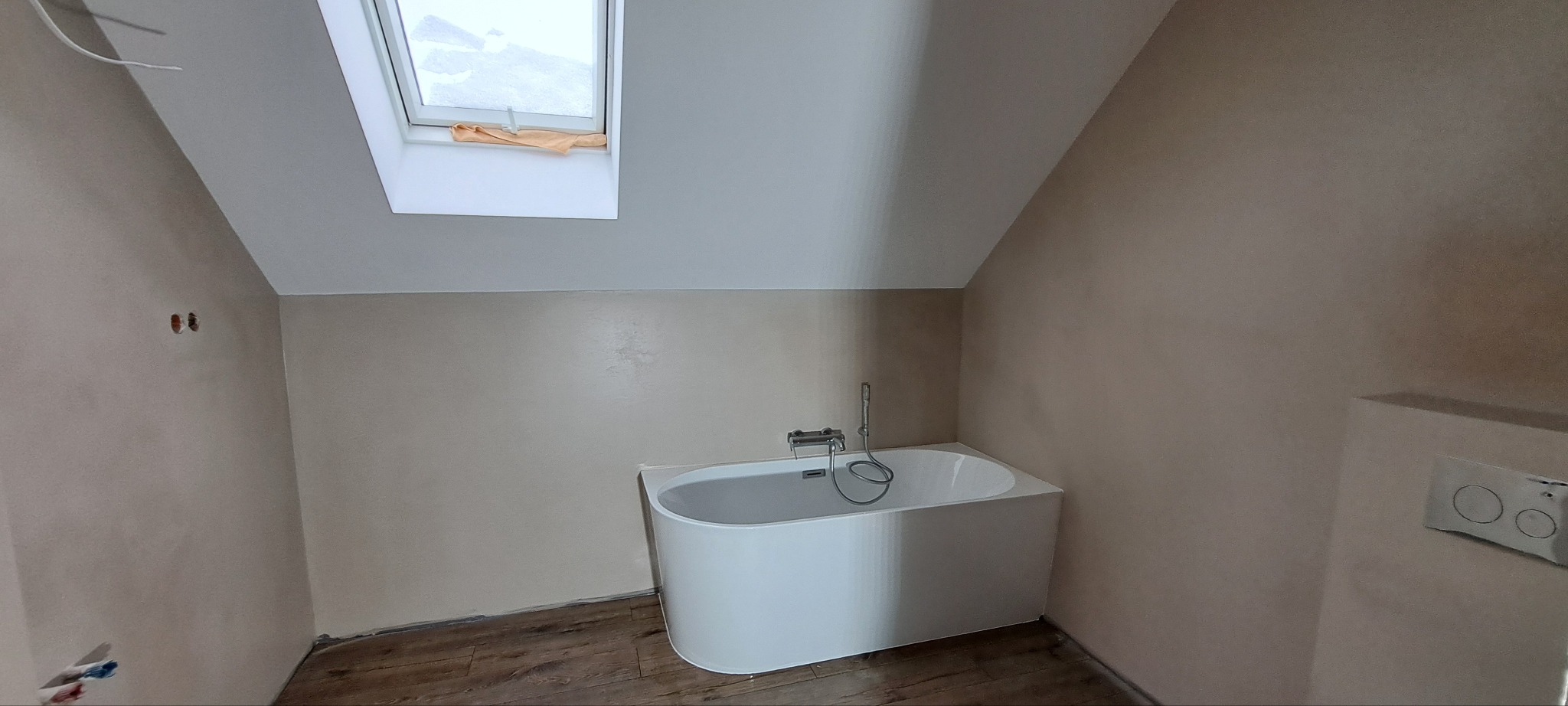 Wykończona łazienka na poddaszu w Złotowie. Widoczna wanna, okno dachowe i gładkie ściany w beżowym odcieniu. Podłoga wyłożona panelami.