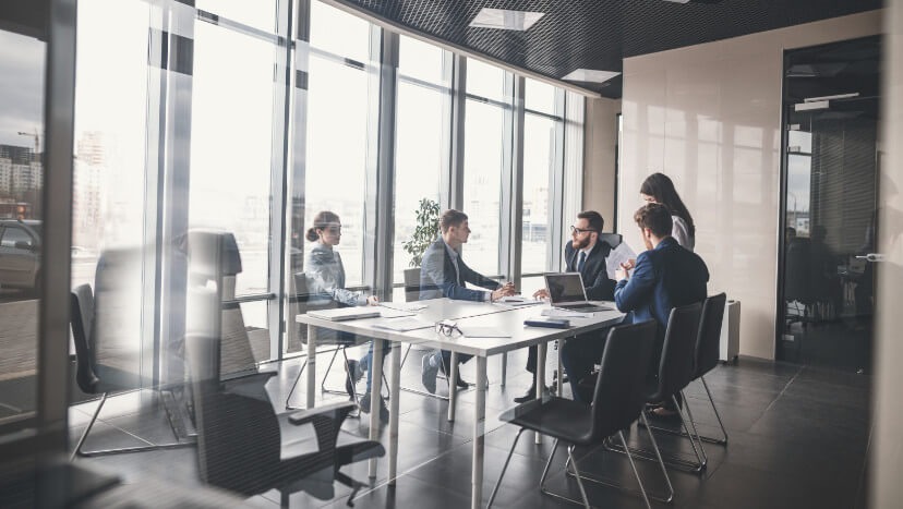 Zespół finansowy w nowoczesnym biurze omawia strategię przy stole konferencyjnym z laptopami, dokumentami i okularami, z widokiem na miasto przez panoramiczne okna.