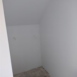 Luxs-Montaż-Bud - Świeżo pomalowane, jasnoszare ściany klatki schodowej w trakcie prac wykończeniowych, widoczne niedoskonałości na schodach i wystające kable ze ściany.